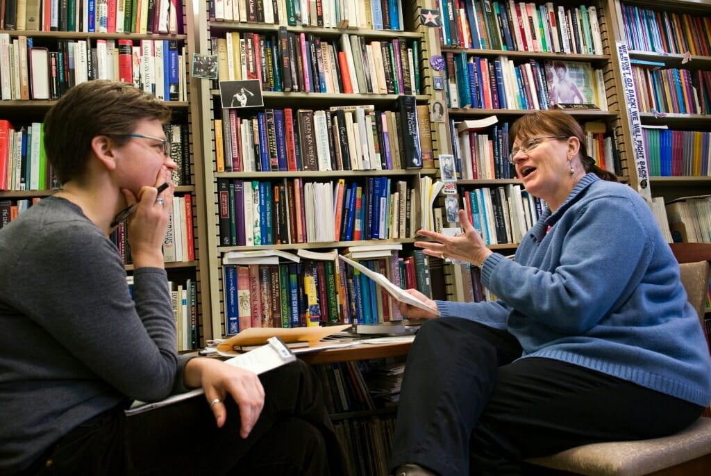 Susan Cook and Jessica Courtier conversing in front of a wall of shelves filled with books