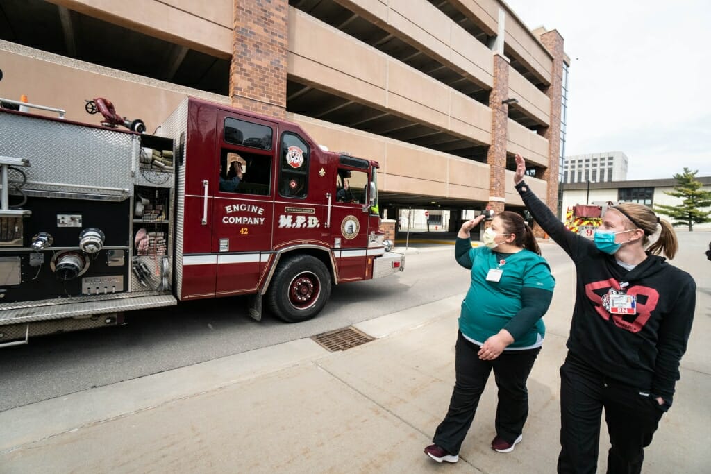 Workers in masks wave at fire truck