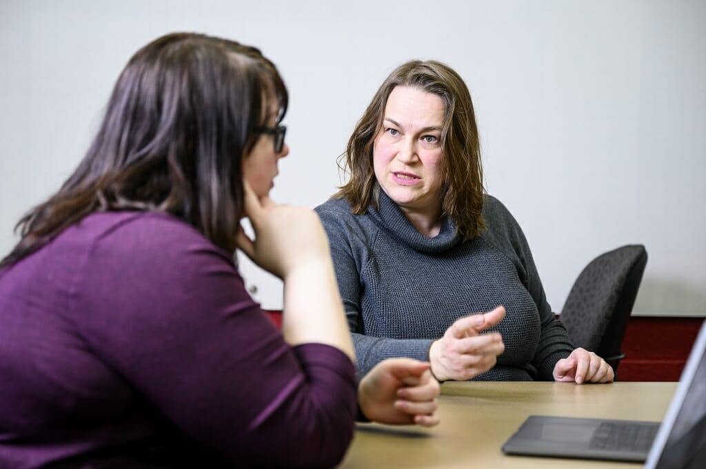 Irena Knezevic, seated at a table, talking to a student