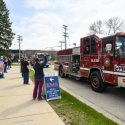 Health care workers standing on sidewalk waving at passing fire engine