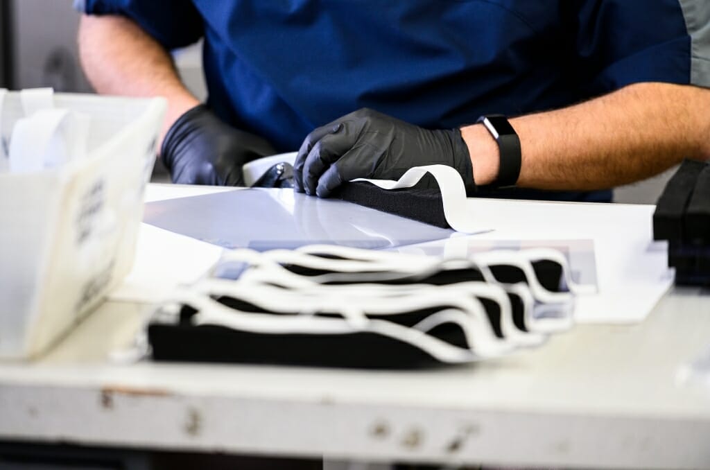 A worker's gloved hands behind a stack of face shields.