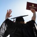 Person in cap and gown raising hands and holding diploma