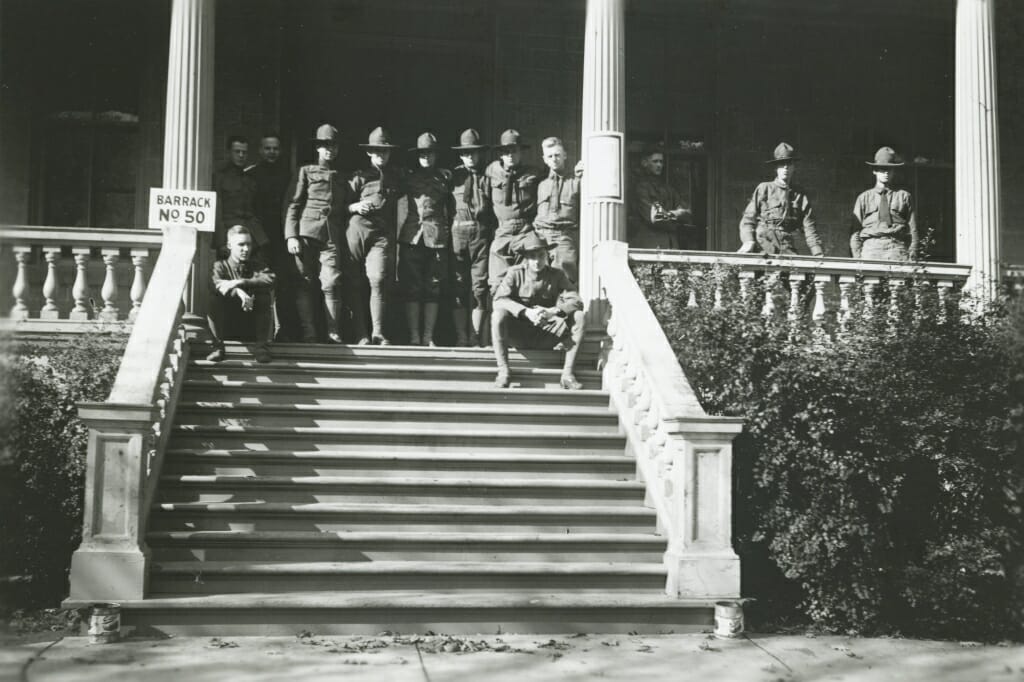 A small group of men in military uniforms standing at the top of the steps to a building