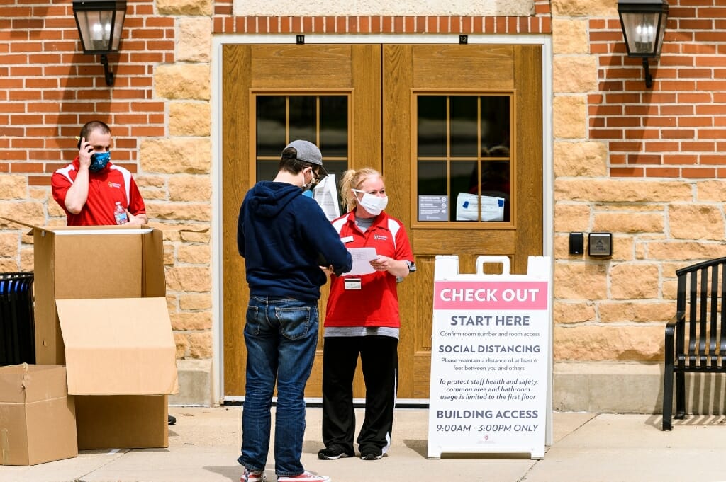 Two people stand outside wooden doors of a residence hall.