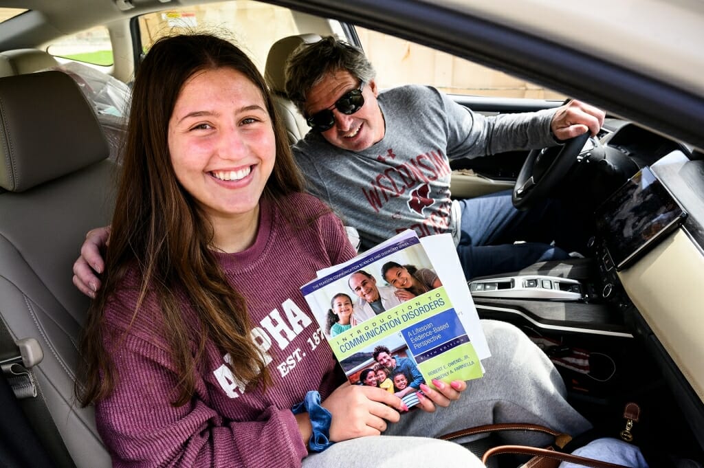 A father and daughter smile out the window of their car.