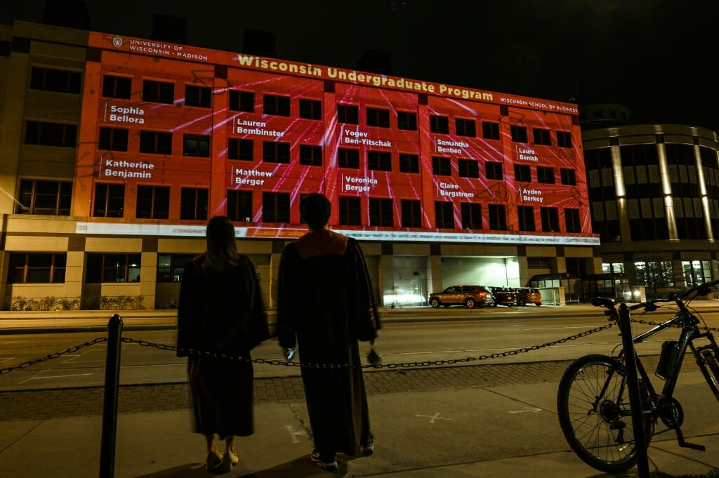 Two people stand watching Grainger Hall with names projected on it.