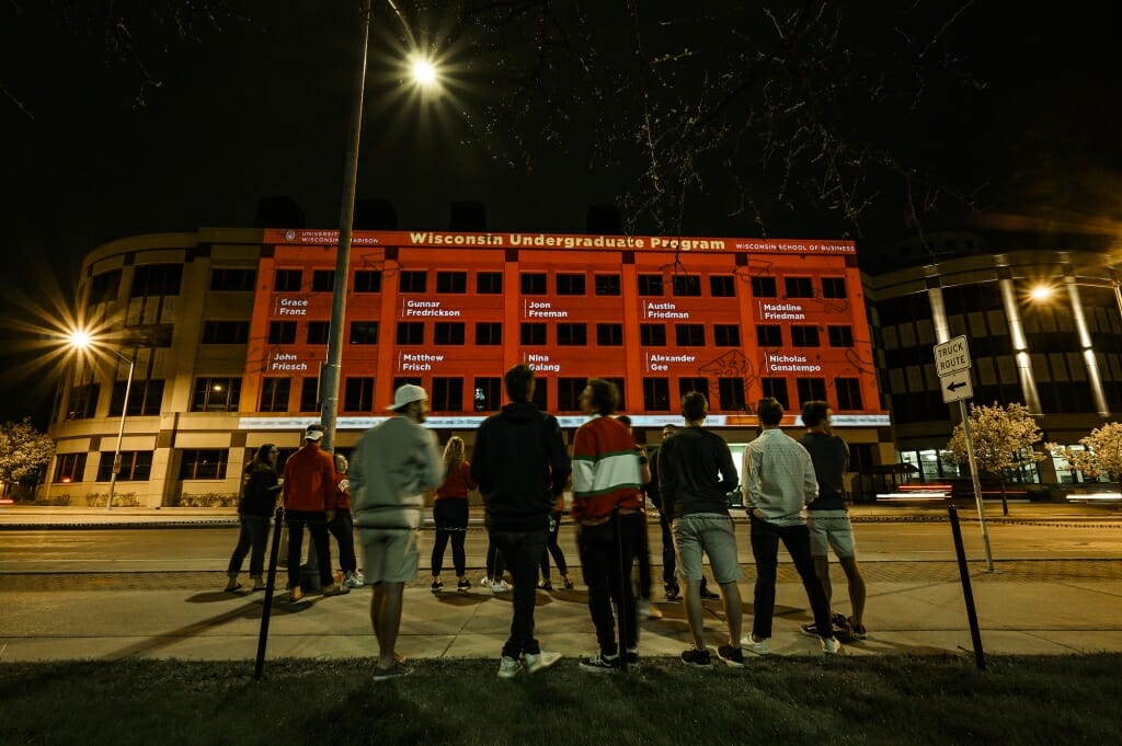 A crowd of people watches the names projected on Grainger Hall.