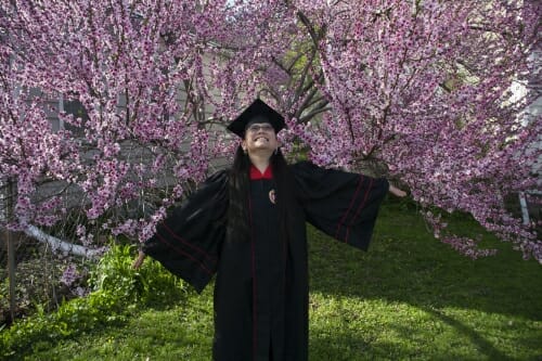 Photo of Laura Yin in her cap and gown in front of a blossoming tree