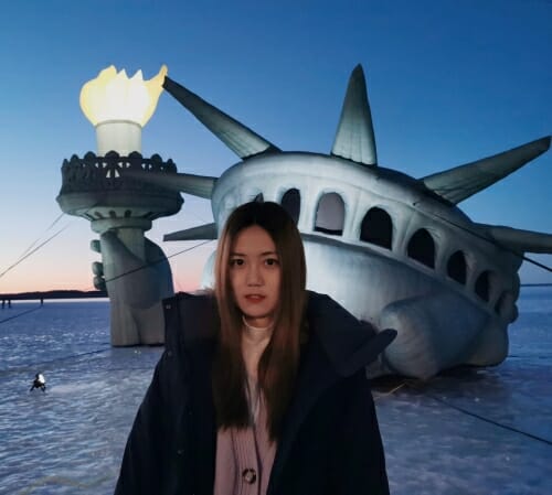 Photo of Runyi Wang in winter on Lake Mendota in front of a statue of Lady Liberty emerging from the ice