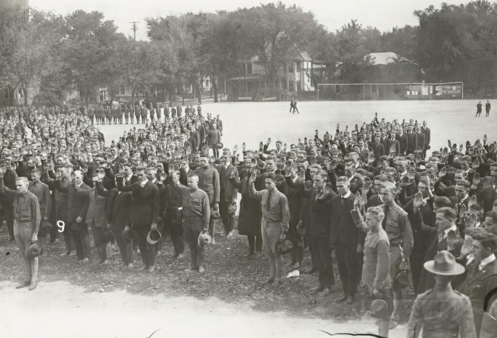 Large group of men in suits and military uniforms raising their right hands