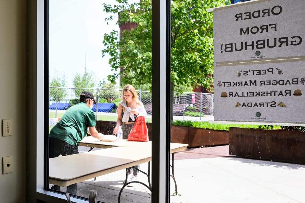 A worker behind a table gives food to someone arriving for pickup.