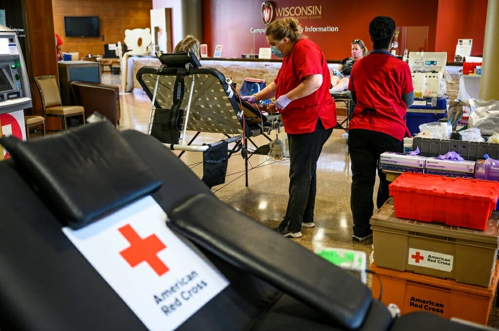 Red-clad Red Cross workers assist a blood donor.