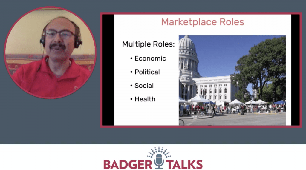 A man speaks on a screen with a photo of a farmers market.