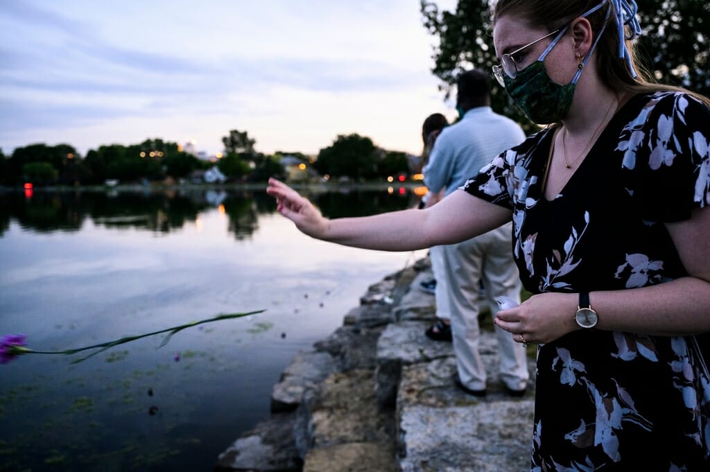 People throw flowers into a lake at dusk.