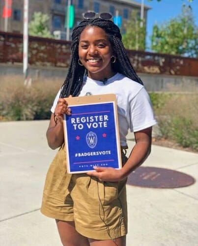 Tamia Fowlkes holding a small sign that says REGISTER TO VOTE