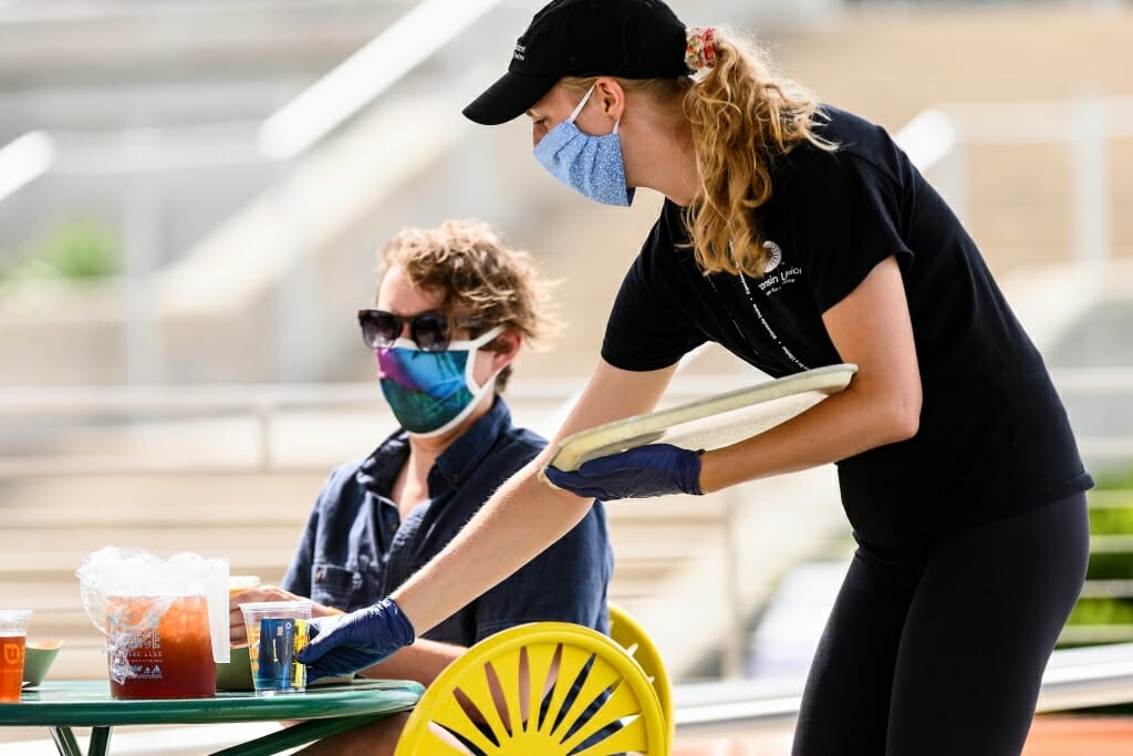 A woman wearing a face mask runs a credit card for a patron seated at a Terrace table.