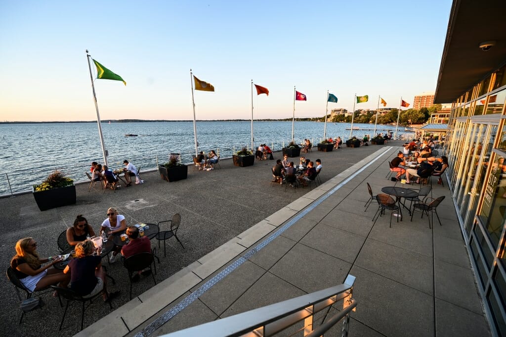 Flags snap in the wind on the Terrace as people enjoy food and drink.