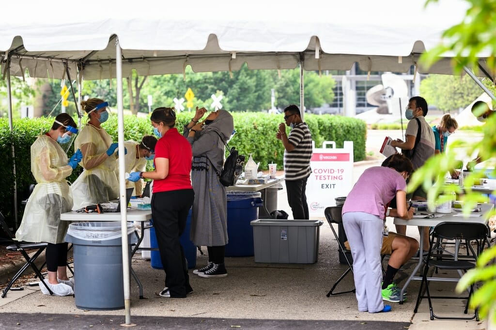 Staff from University Health Services instruct people how to self-administer a nasal-swab test at a COVID-19 testing tent set up on Henry Mall.