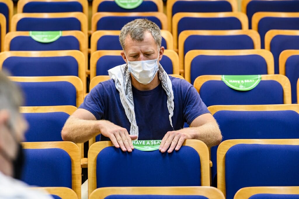 Staff member Donovan Kron places a seating location sticker on a seat back in a reconfigured lecture hall.