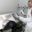 Photo of two staff members in protective lab gear standing next to a large centrifuge.