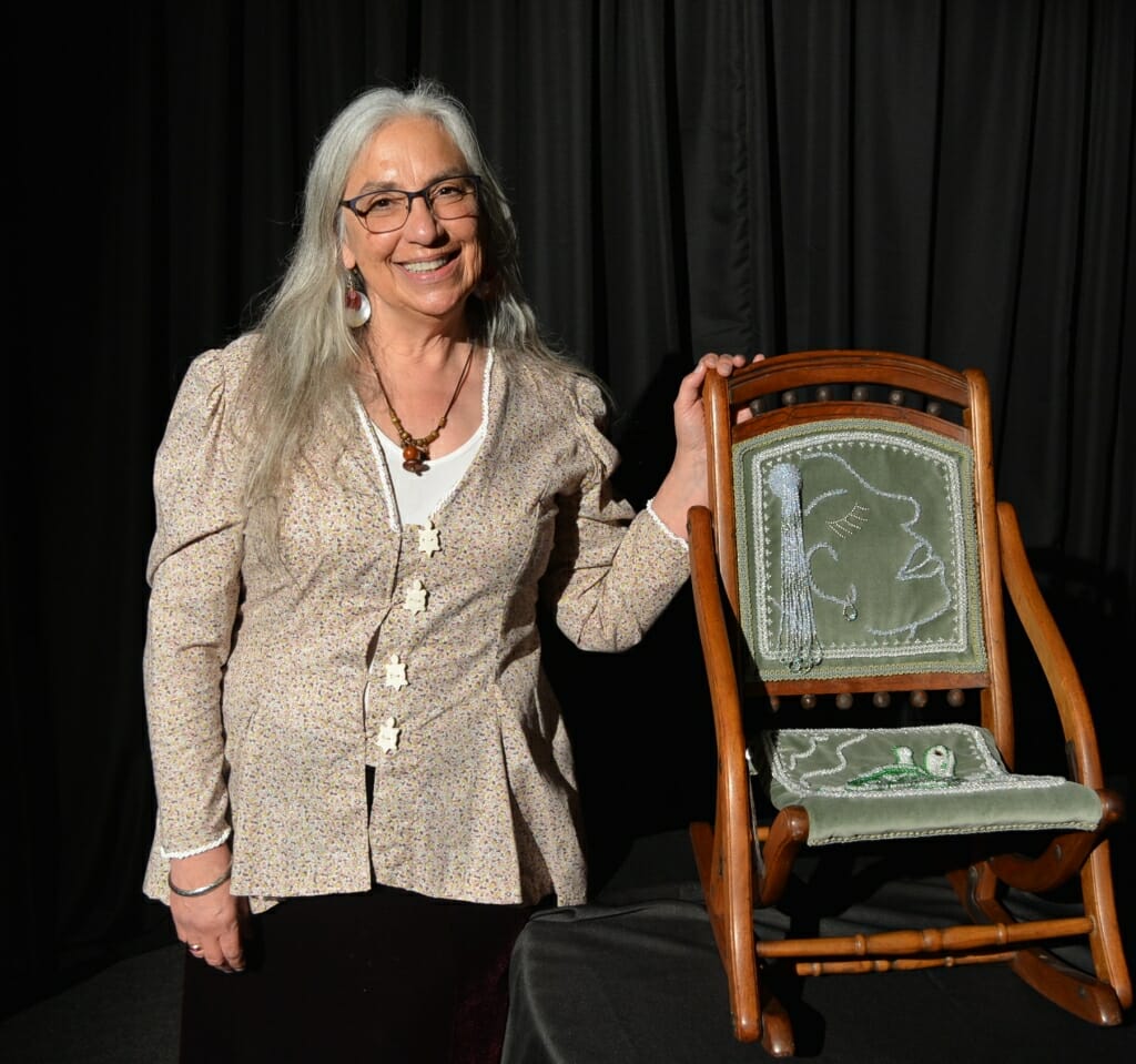 A woman stands next to a beaded chair.