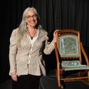 A woman stands next to a beaded chair.