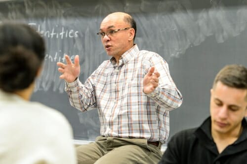 Thornton sitting in front of a chalkboard, gesturing and speaking