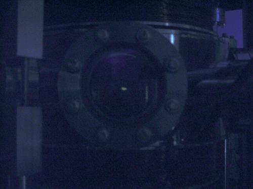 The chamber in the dark shows faintly glowing rubidium atoms at the center