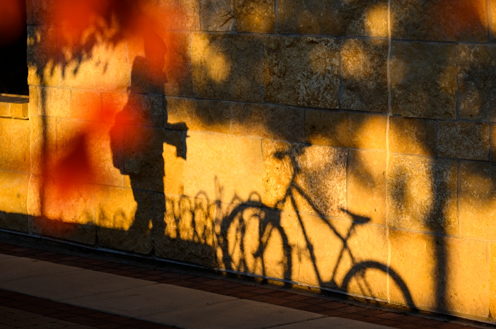 Late afternoon shadows of a parked bike and a passing pedestrian are cast upon the stone exterior of the Gordon Dining and Event Center.