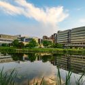 A photo of the exterior of a mid-rise research building as seen across a pond on a bright sunny day in summer.