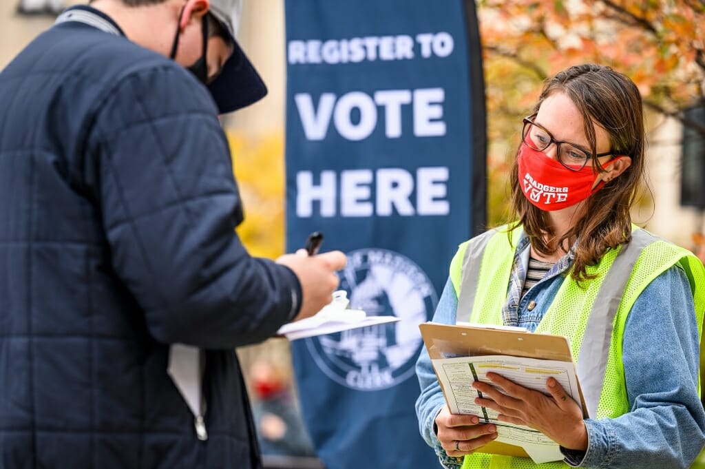 Ann Elise Trafford, with the City of Madison Clerk’s Office, right, helps students register to vote.