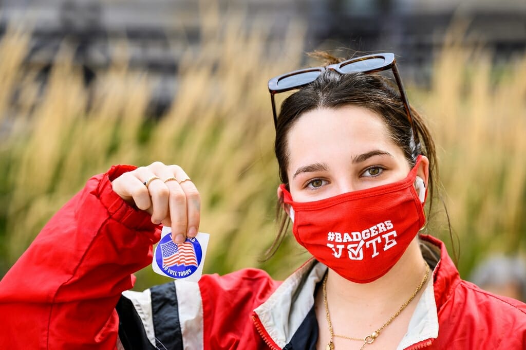 Maddie Stein, a first-year student from Los Angeles, shows a sticker and Badgers Vote mask after registering to vote with City of Madison Clerk’s Office staff working an information table on East Campus Mall.