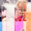 Scientist's face behind beakers of colorful liquids