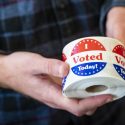 Wearing face masks and maintaining physical distance from others, UW students cast their ballots at the Chazen Museum of Art polling station at the University of Wisconsin-Madison on November 3, 2020. Here, a poll worker hands out I voted stickers to students after they cast their ballot. (Photo by Bryce Richter / UW-Madison)