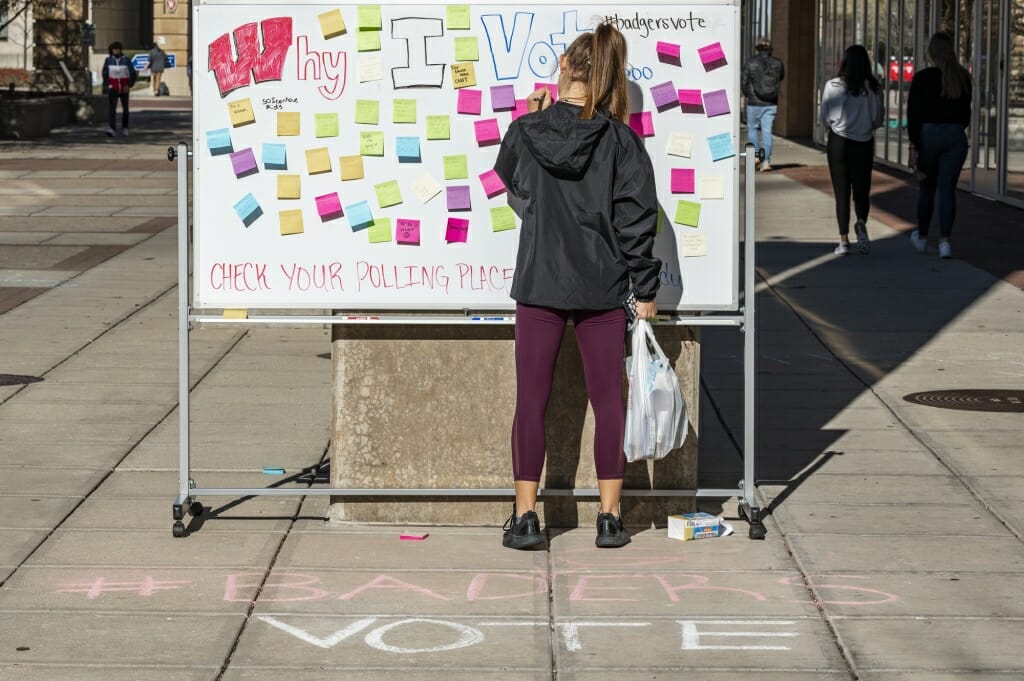 Students write down the reasons why they vote at an interactive display outside of 333 East Campus Mall.