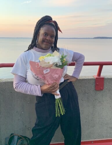 Christiana Fowlkes posing holding flowers leaning on a railing next to lake