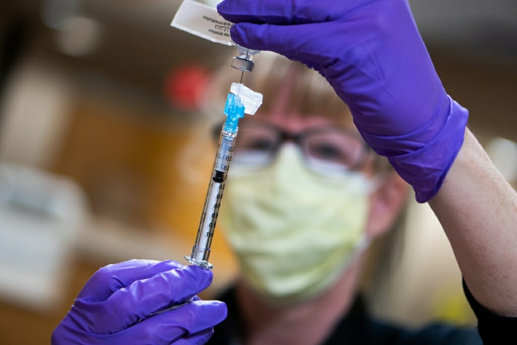 Person wearing mask and rubber gloves holding up a syringe