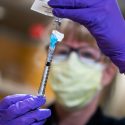 Person wearing mask and rubber gloves holding up a syringe