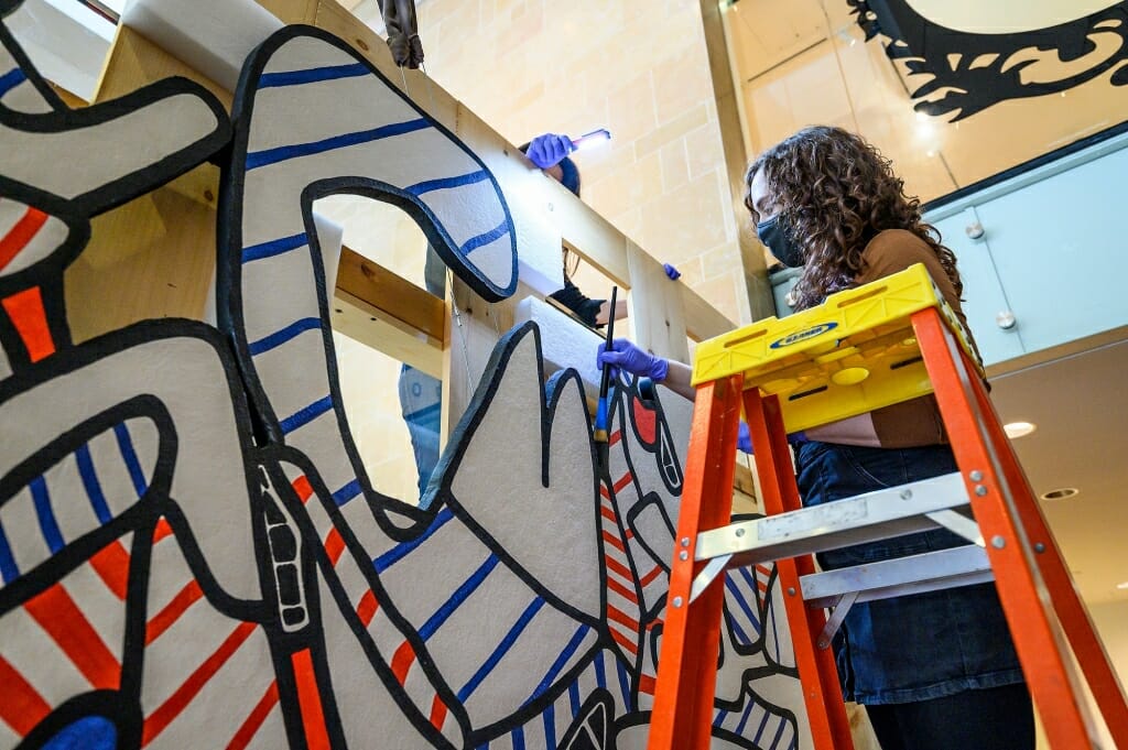 Museum employee Emma Shoer uses an artist's brush to dust the edges of the artwork.