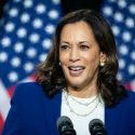 Harris standing in front of American flags and speaking into microphones