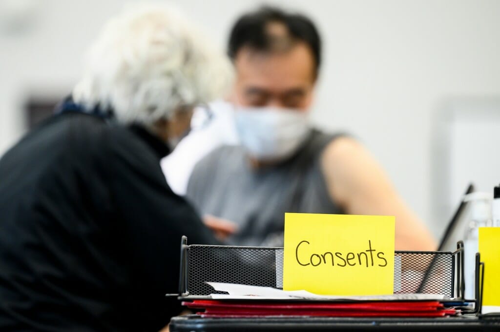 A stack of medical consent forms is pictured as University Health Service nurse practitioner Linda Johnson vaccinates Akihiro Ikeda, a genetics professor.