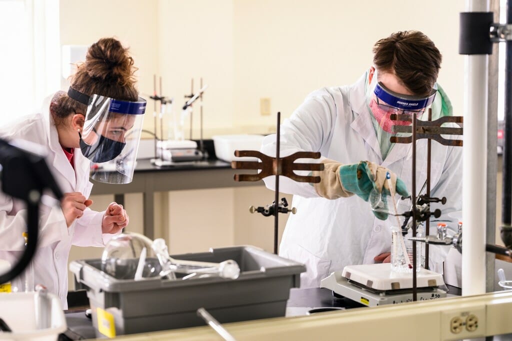 Taking turns, student Abi Schmeiser, at left, leans in for a physically distanced look as lab partner Donald Richards conducts an experiment in Chemistry 329.