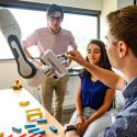 Graduate students David Porfirio (left), Bengisu Cagiltay (center) and Andrew Schoen (right) work with a robotic arm in the Wisconsin Human-Computer Interaction Lab located in the Computer Science Building.