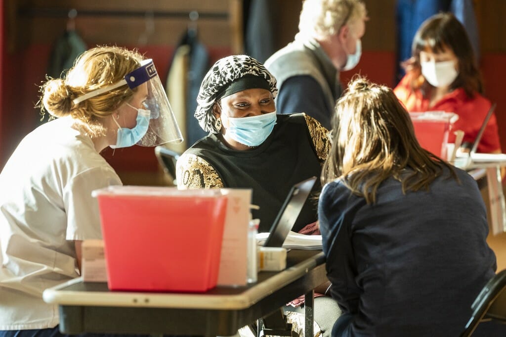 Photo of School of Nursing faculty supervisor Madelyne Greene (right) and nursing student Ariahna Grossenbacher (left) talking to custodian Selle Fall (center) about COVID-19 vaccination before Selle receives her shot.