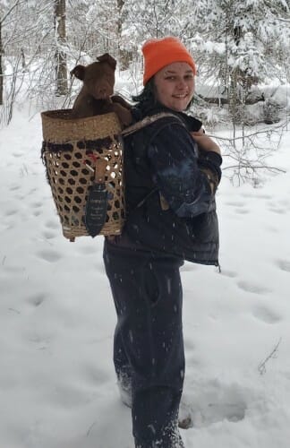 Abi Fergus standing in the snow with a dog in a basket on her back