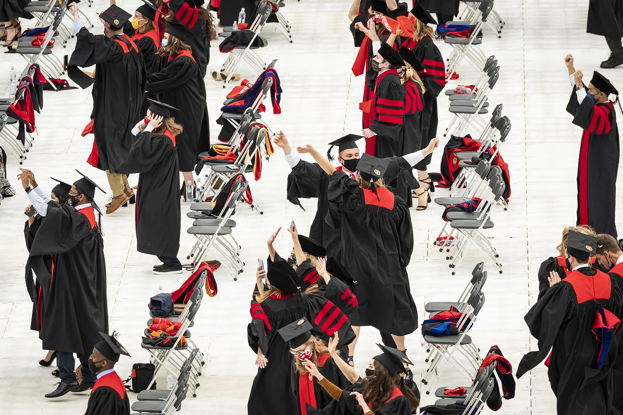 Graduates in caps and gowns hold hands and dance on the field at Camp Randall.