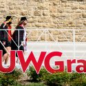 Photo of two women in caps and gowns walking past a giant sign spelling out 