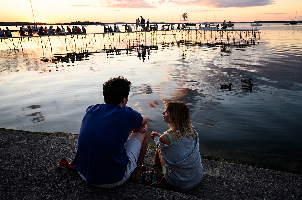 Two people look out over the lake, with a pier in the background with more people on it.