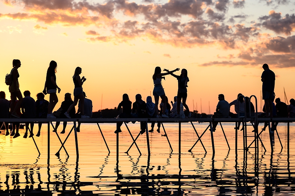 People are silhoutted by the setting sun as they sit on a pier in Lake Mendota.