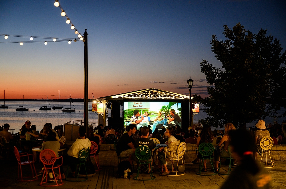 A movie is projected on a screen on the Memorial Union Terrace, with the lake in the background.